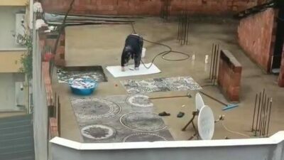 Bursa’da su kesintisi yapılırken, yağmur altında hortumla halı yıkayan bir