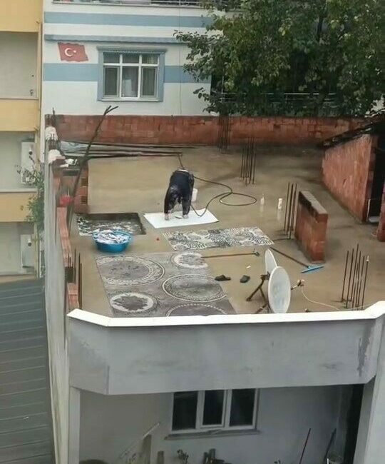 Bursa’da su kesintisi yapılırken, yağmur altında hortumla halı yıkayan bir